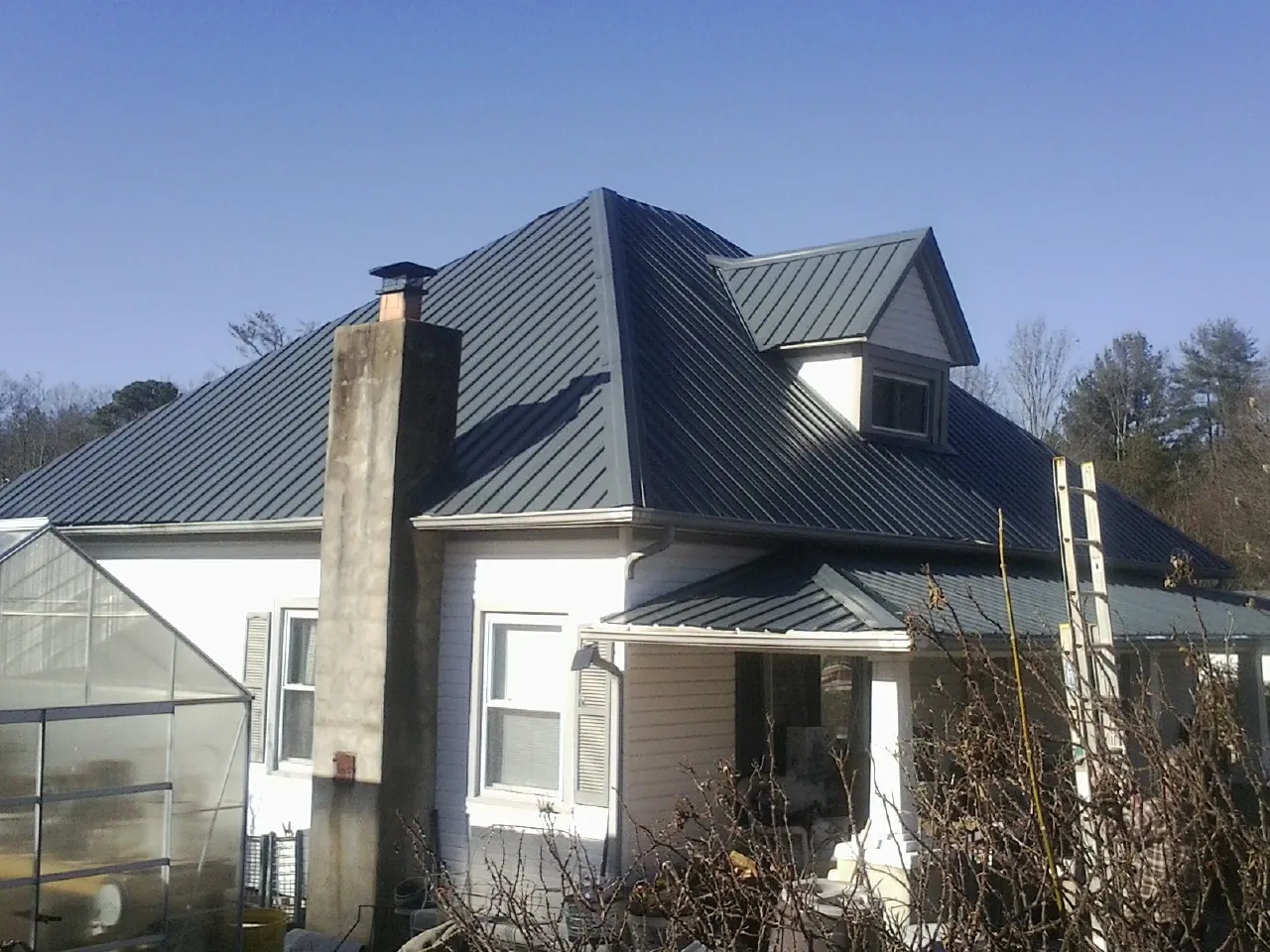 Dark blue standing seam metal roof on a white farmhouse with dormer — Slate & Tile Roof Repair by Roofing Brothers in Muldrow