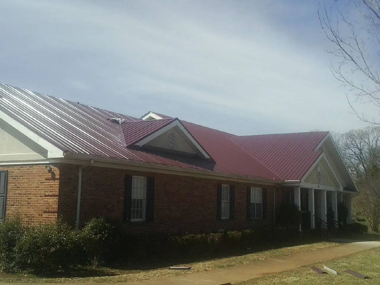 Red metal roof with gabled entries on a long brick building, from a Hail Damage Roof Repair job in Muldrow