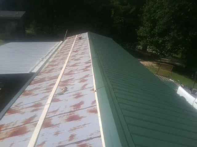 Old rusted panels beside newly installed green metal roofing — Wind Damage Roof Repair by Roofing Brothers in Muldrow