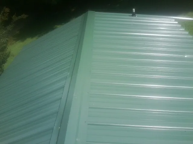 New green metal panels meeting at the ridge of a roof — Flat Roof Repair work by our crew in Muldrow
