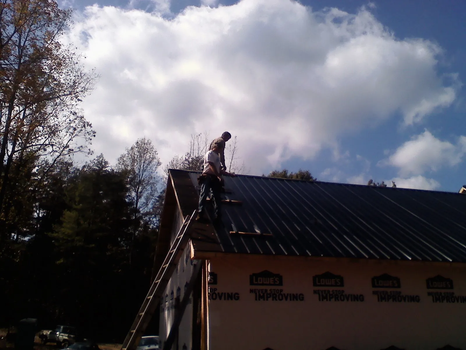 Roofer fastening dark metal panels high against a cloudy sky, from a Roof Inspection job in Muldrow