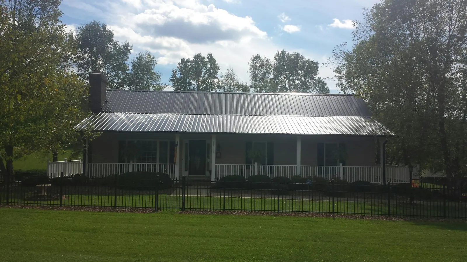Gray metal roof on a brick ranch with a full width front porch — Gutter Guard Installation work by our crew in Muldrow