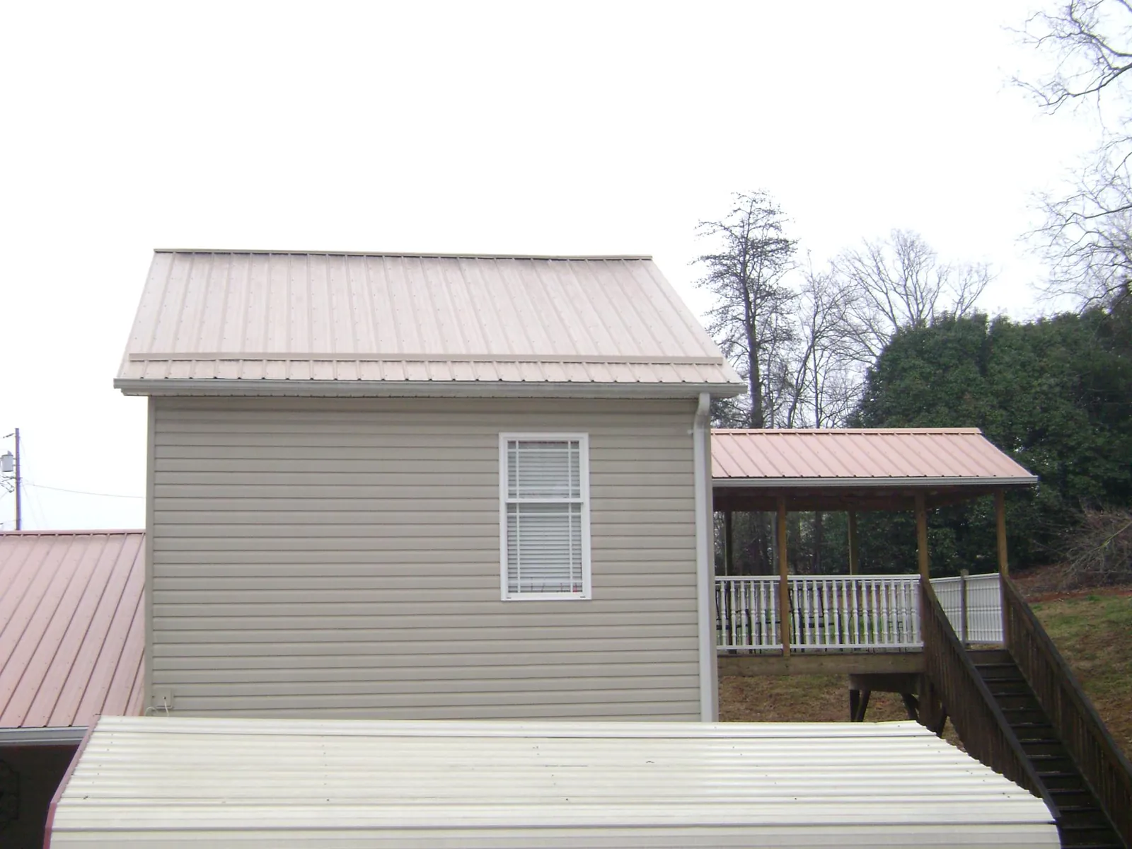 Tan metal roofs on a two story addition and attached porch, from a Roof Replacement job in Muldrow