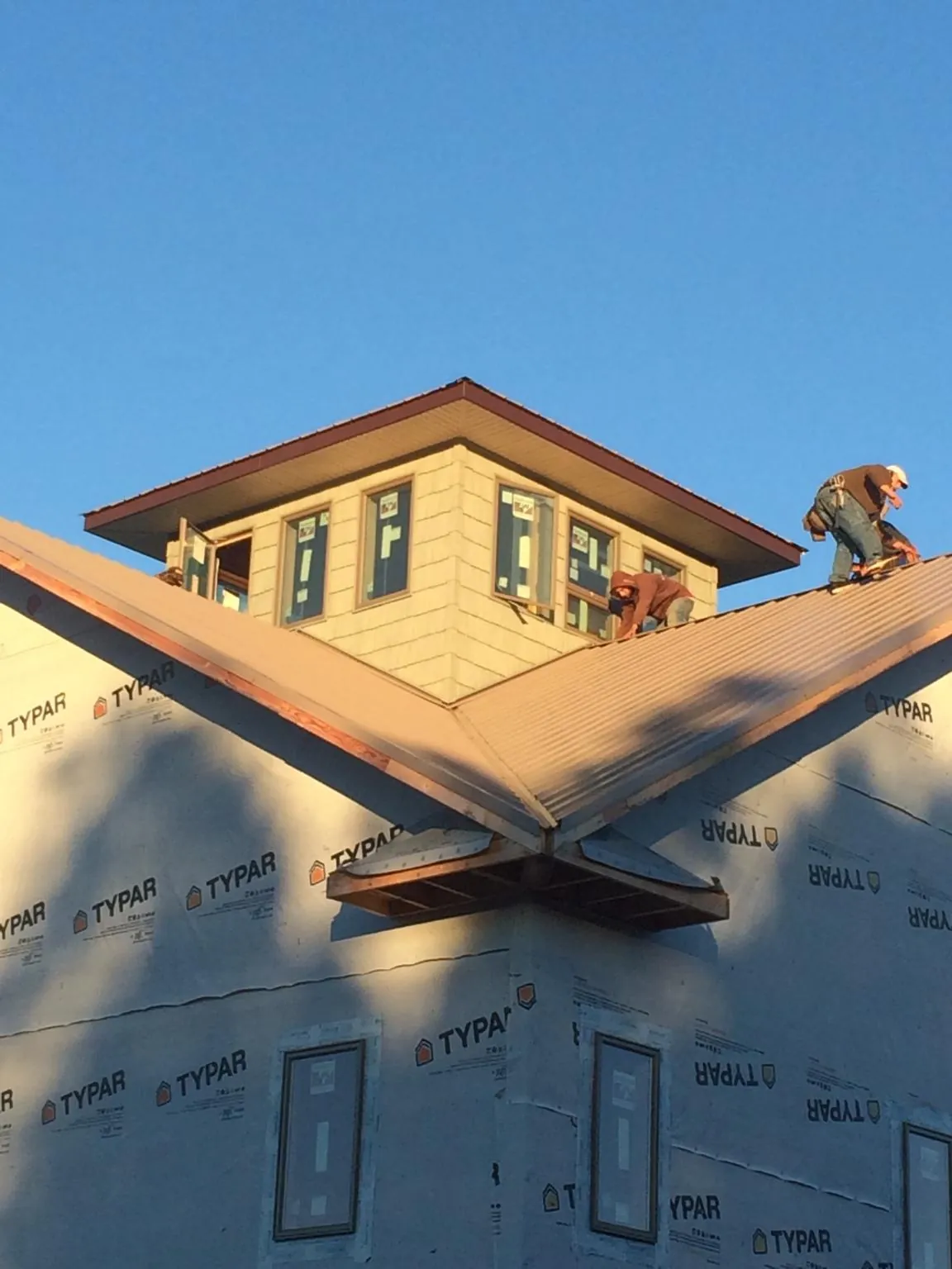 Roofers working around a rooftop cupola on a new metal roof at sunset — Roof Waterproofing in Muldrow by Roofing Brothers